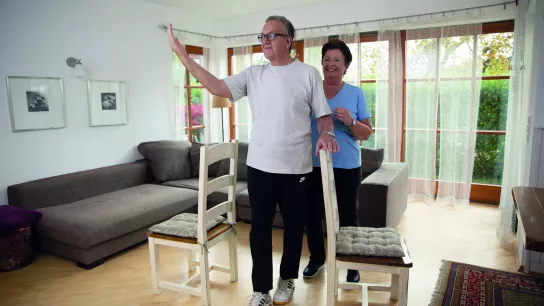 © ÖGK/Yvonne Kreuzmayr älterer Mann bei einer Bewegungsintervention in einer Wohnung mit einer älteren Dame